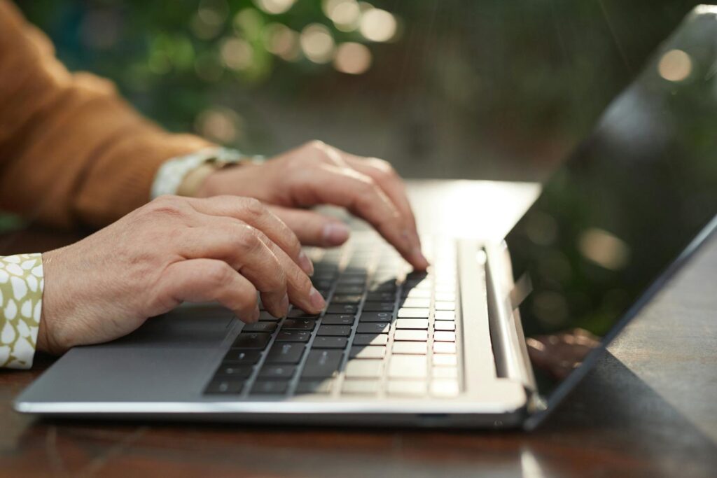 Vagas Remotas para Atendimento e mais em Healthtech Close-up of hands typing on a laptop outdoors with natural background and sunlight.
